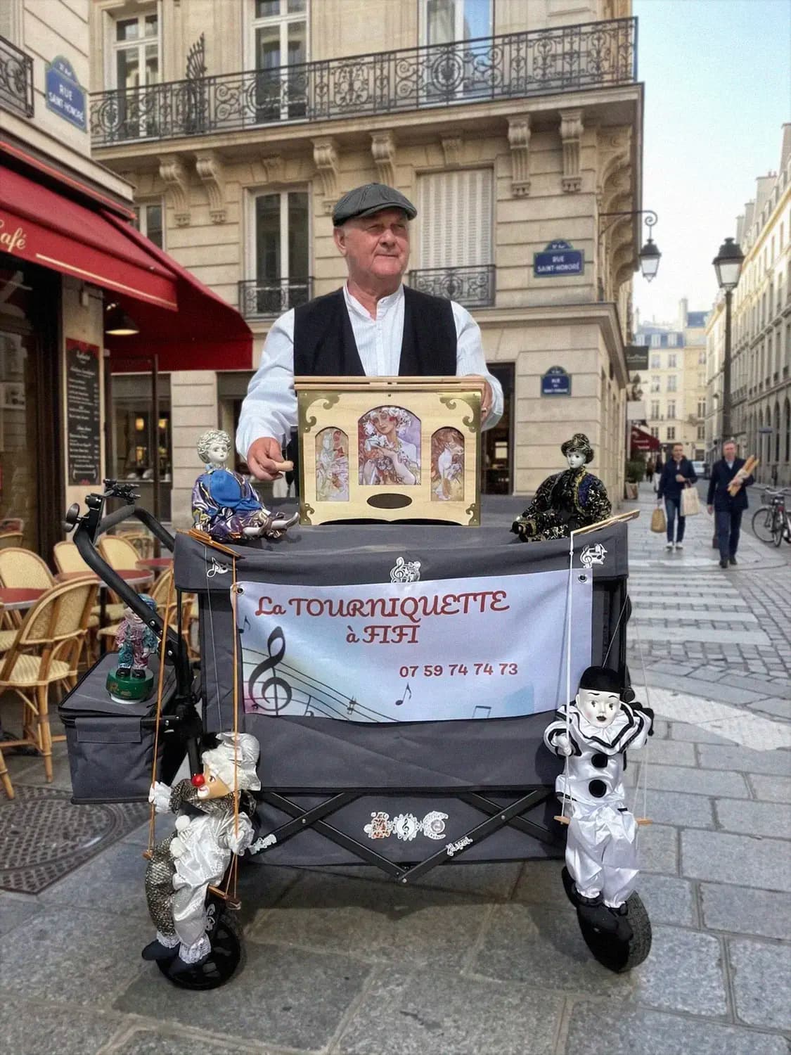 Photo réaliste d'un homme en tenue traditionnelle (gilet noir, chemise blanche et casquette) manipulant un orgue de Barbarie nommé 'La Tourniquette à Fifi'. Il est installé sur une rue pavée typique de Paris, avec des façades d'immeubles haussmanniens et la terrasse d'un café rouge en arrière-plan.
